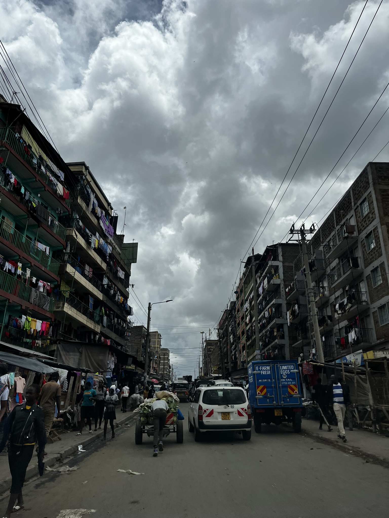 Busy residential street with handcart, vehicles and market stalls